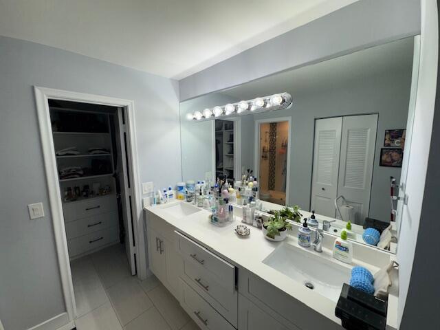 full bathroom with tile patterned flooring, double vanity, a spacious closet, and a sink