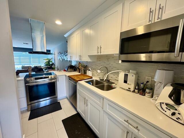 kitchen featuring a sink, decorative backsplash, light countertops, stainless steel appliances, and island range hood