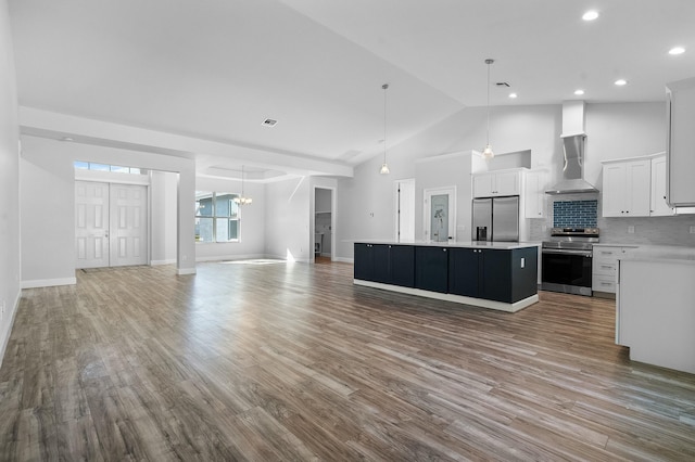 kitchen featuring wall chimney range hood, open floor plan, a center island, appliances with stainless steel finishes, and light countertops