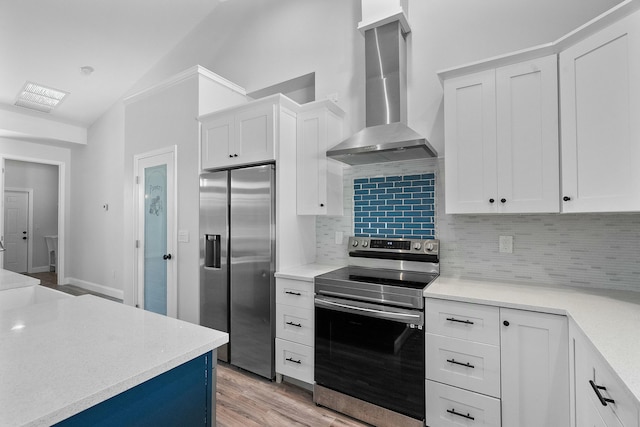 kitchen with wall chimney range hood, appliances with stainless steel finishes, white cabinets, light wood finished floors, and decorative backsplash