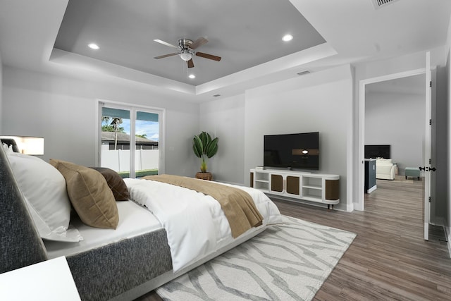 bedroom with a raised ceiling, recessed lighting, wood finished floors, and visible vents