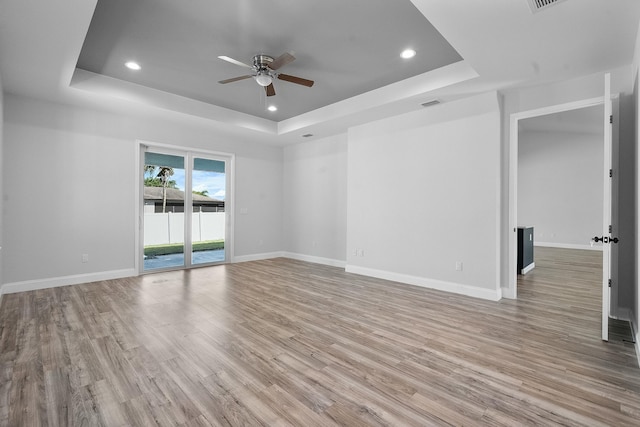 empty room featuring a raised ceiling, light wood-style floors, and baseboards