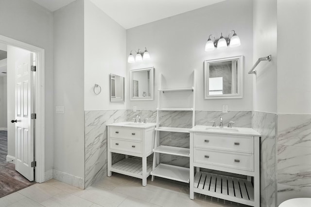 bathroom with wainscoting, tile walls, two vanities, and a sink