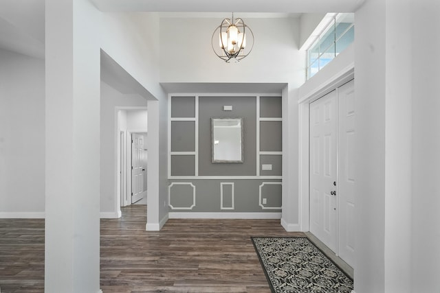 entrance foyer with dark wood-style floors, a chandelier, a high ceiling, and baseboards