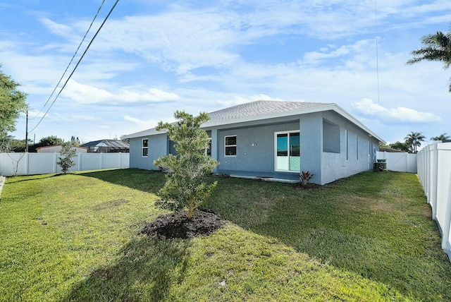 back of house with stucco siding, a lawn, a fenced backyard, and a shingled roof