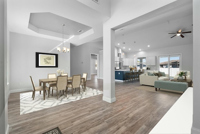 dining space featuring visible vents, wood finished floors, baseboards, a raised ceiling, and a towering ceiling