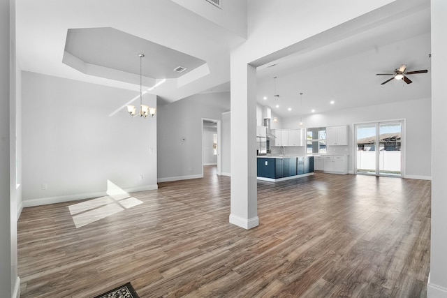 unfurnished living room featuring visible vents, ceiling fan with notable chandelier, dark wood finished floors, baseboards, and a towering ceiling