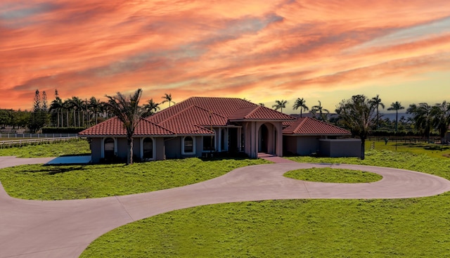 mediterranean / spanish home featuring a tiled roof, curved driveway, a front yard, and fence