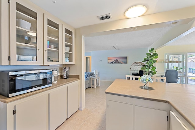 kitchen with visible vents, light countertops, glass insert cabinets, white cabinetry, and stainless steel microwave