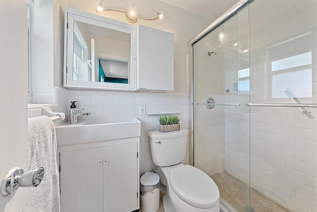 bathroom with a shower stall, tile walls, vanity, and toilet