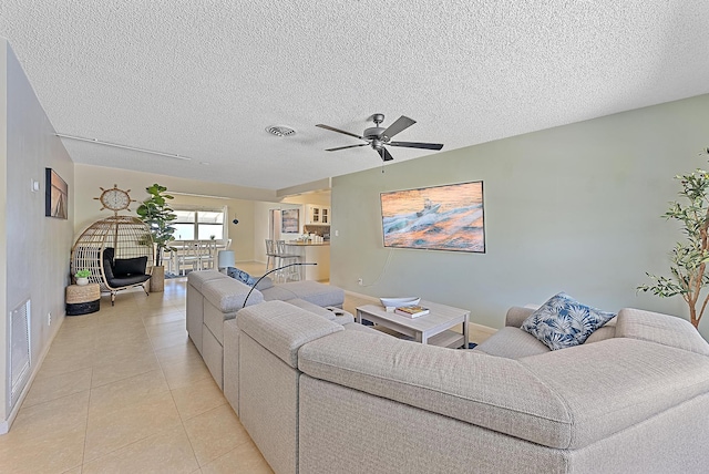 living area with light tile patterned floors, a ceiling fan, visible vents, and a textured ceiling