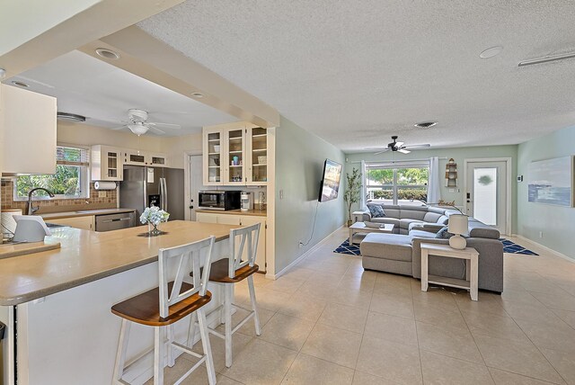 kitchen featuring a peninsula, open floor plan, glass insert cabinets, appliances with stainless steel finishes, and tasteful backsplash