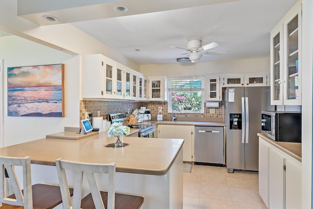 kitchen with light tile patterned floors, a peninsula, a sink, appliances with stainless steel finishes, and backsplash