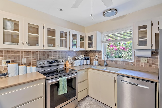 kitchen featuring a sink, stainless steel appliances, light countertops, glass insert cabinets, and backsplash