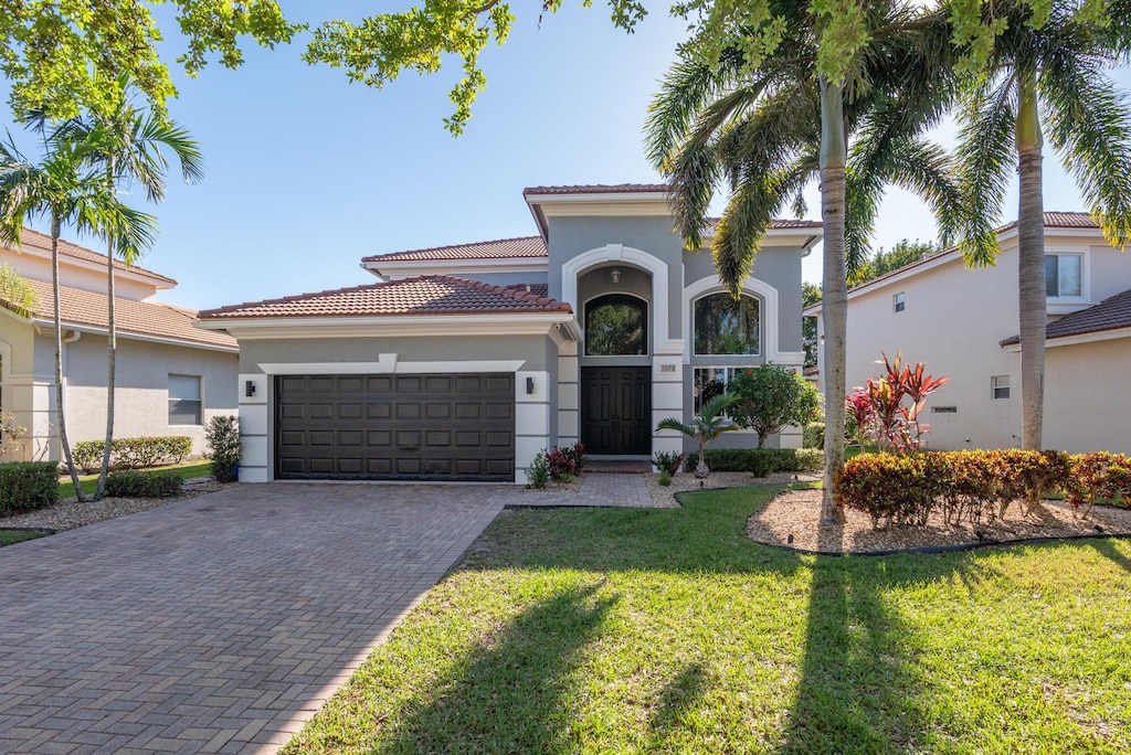 mediterranean / spanish-style home featuring a front yard, decorative driveway, a garage, and stucco siding