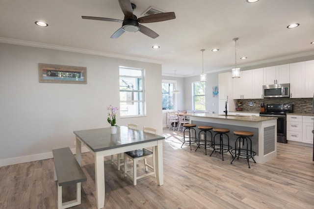 kitchen with light wood finished floors, stainless steel microwave, electric range oven, decorative backsplash, and a kitchen island with sink