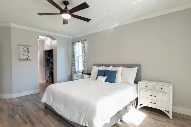 bedroom featuring a walk in closet, ornamental molding, wood finished floors, arched walkways, and baseboards