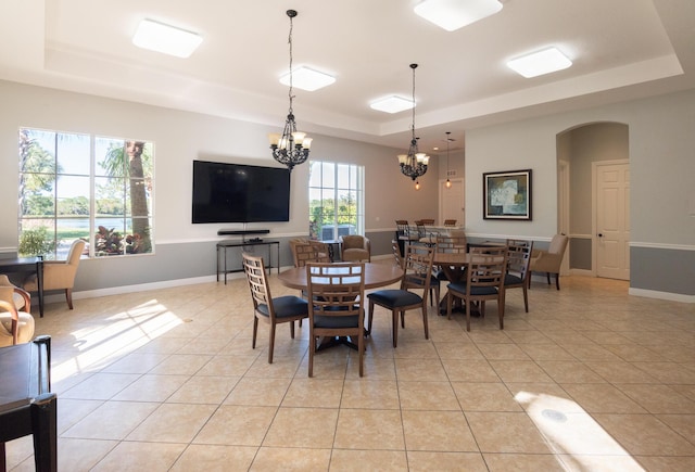 dining area featuring baseboards, a chandelier, light tile patterned floors, arched walkways, and a raised ceiling