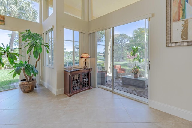 doorway to outside with tile patterned flooring, a high ceiling, and baseboards