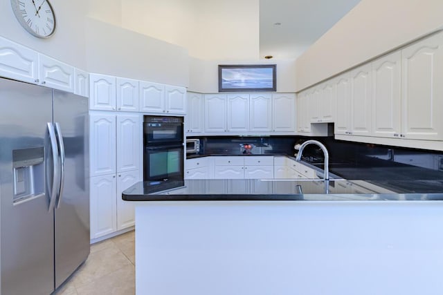 kitchen with stainless steel fridge, a peninsula, light tile patterned flooring, and white cabinetry