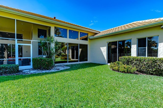 rear view of property featuring a lawn, a sunroom, and stucco siding