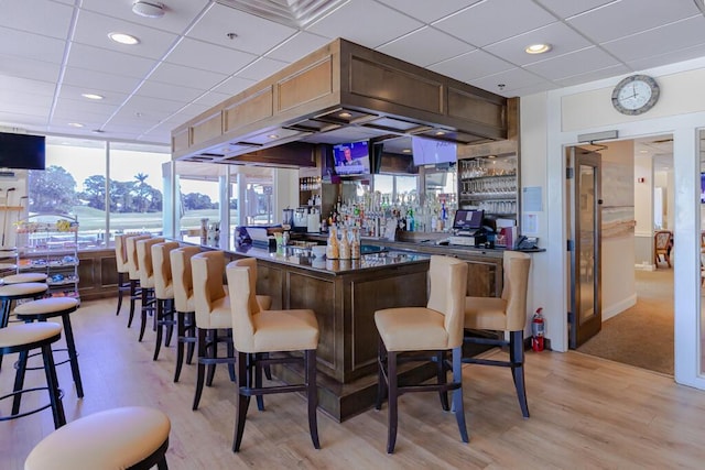 bar with a bar, a paneled ceiling, and light wood finished floors