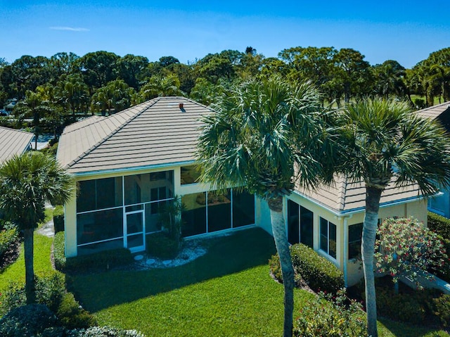 rear view of house with a yard, a tile roof, stucco siding, and a sunroom