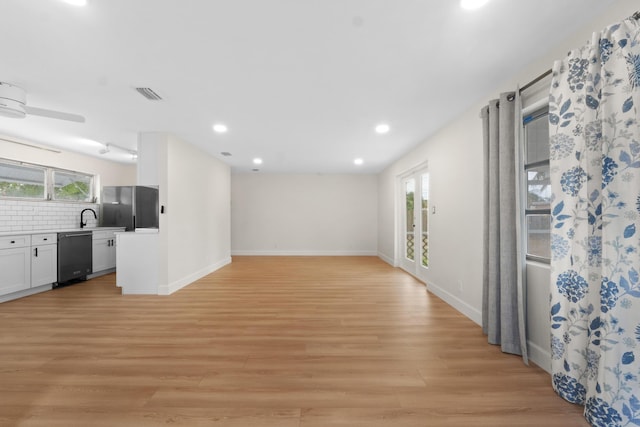 unfurnished living room featuring healthy amount of natural light, light wood finished floors, recessed lighting, a sink, and baseboards