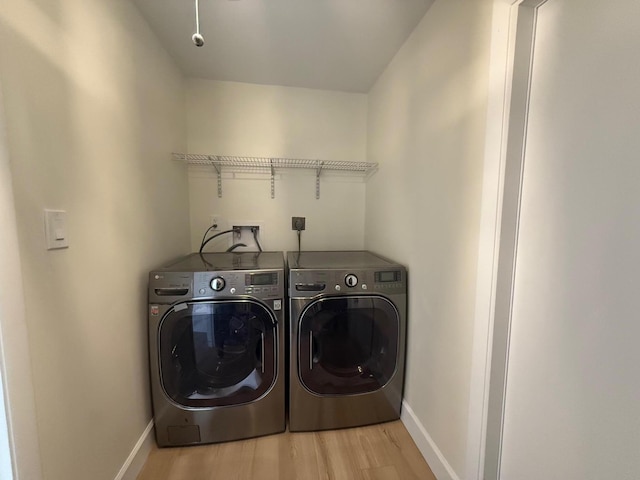 laundry room with laundry area, wood finished floors, washing machine and dryer, and baseboards