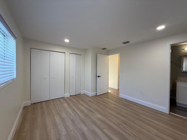 unfurnished bedroom with visible vents, multiple closets, light wood-style floors, and baseboards