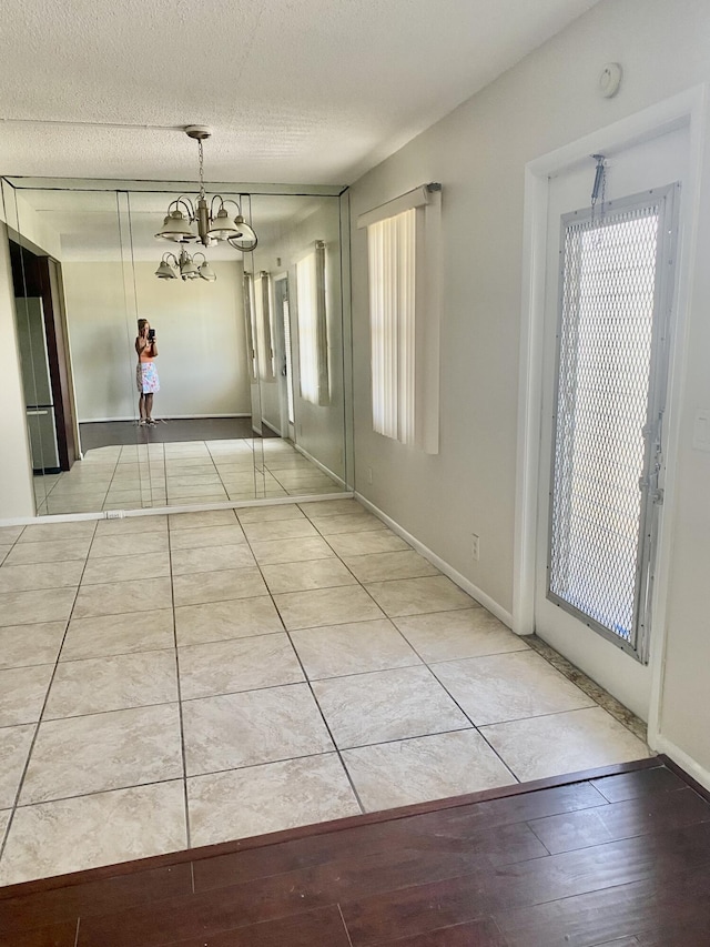 interior space featuring an inviting chandelier, light tile patterned floors, baseboards, and a textured ceiling