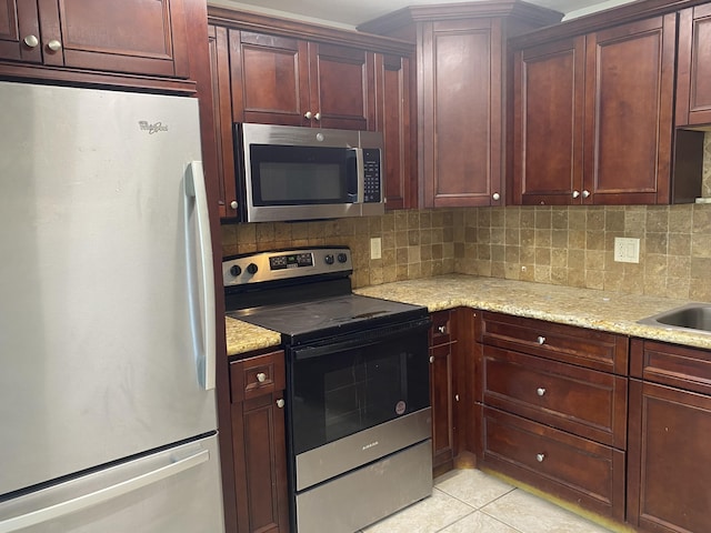 kitchen featuring light stone counters, light tile patterned floors, stainless steel appliances, dark brown cabinets, and backsplash