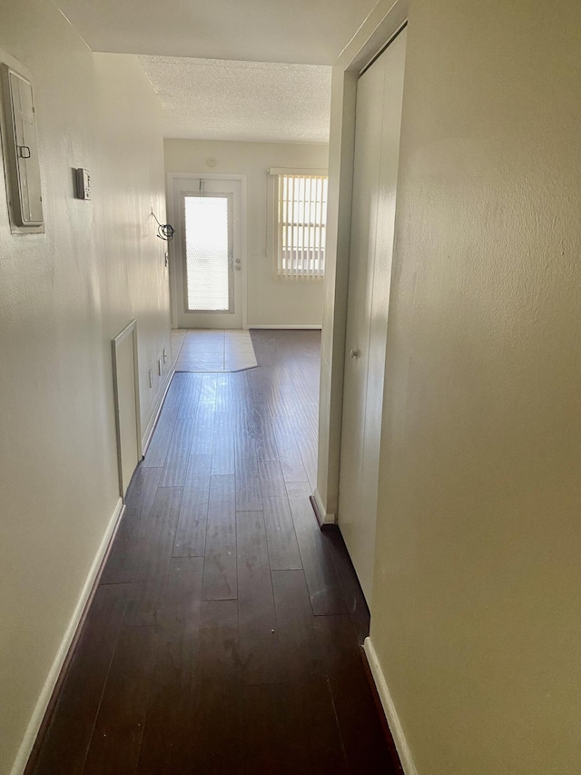 hall with dark wood finished floors, baseboards, a textured ceiling, and electric panel