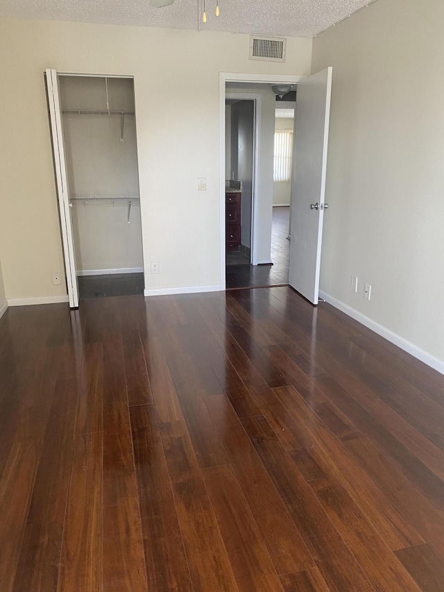 unfurnished bedroom featuring baseboards, visible vents, dark wood finished floors, a closet, and a textured ceiling