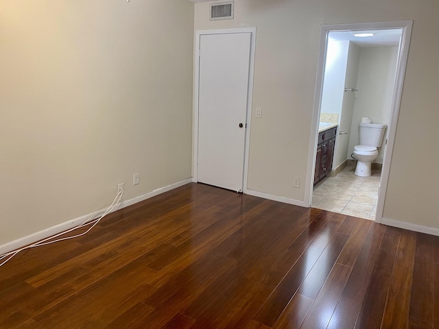 unfurnished bedroom featuring visible vents, ensuite bathroom, baseboards, and hardwood / wood-style flooring