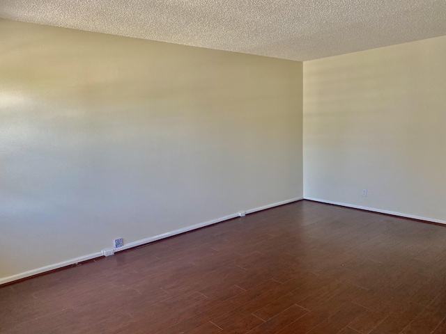 spare room featuring baseboards, dark wood-style flooring, and a textured ceiling