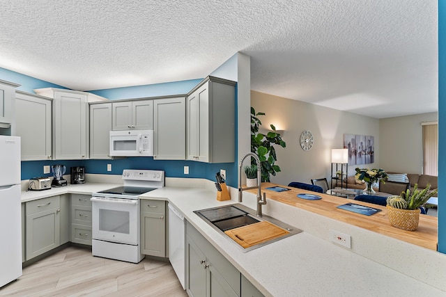 kitchen with a sink, white appliances, gray cabinets, and light countertops