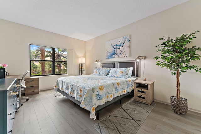 bedroom featuring baseboards, a textured ceiling, and wood finished floors