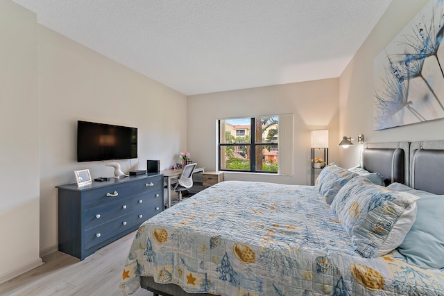 bedroom with baseboards, a textured ceiling, and light wood-style floors