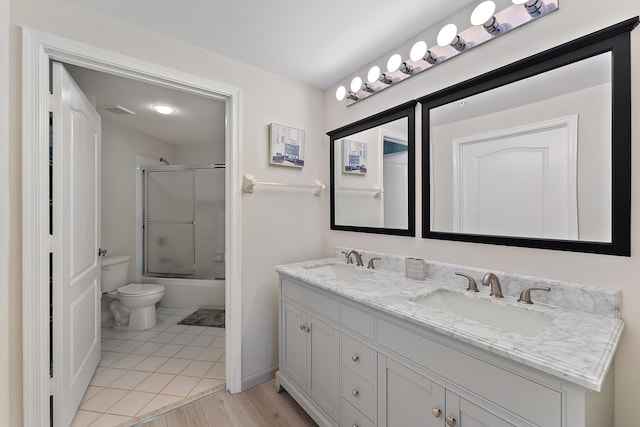 bathroom featuring a sink, bath / shower combo with glass door, toilet, and double vanity