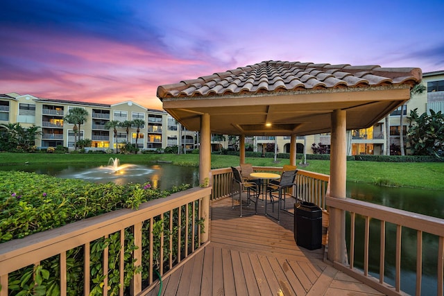 deck at dusk featuring outdoor dining space, a gazebo, a yard, and a water view