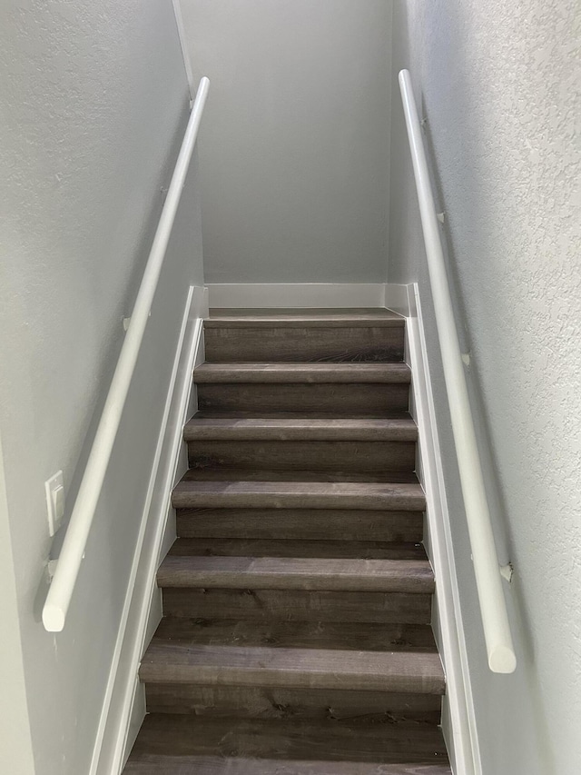 stairway featuring wood finished floors and a textured wall