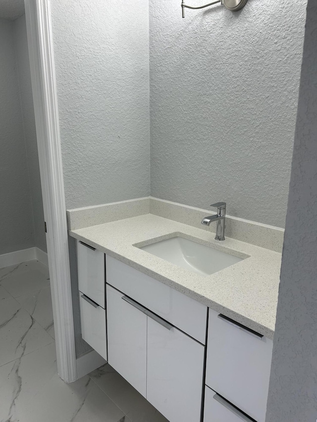 bathroom with marble finish floor, vanity, and a textured wall