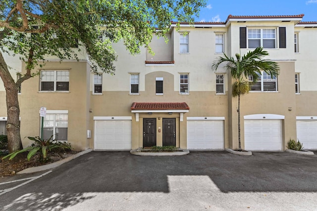 multi unit property with stucco siding, a garage, driveway, and a tiled roof