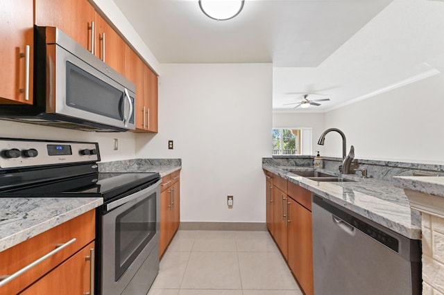 kitchen featuring light stone countertops, appliances with stainless steel finishes, light tile patterned flooring, brown cabinetry, and a sink