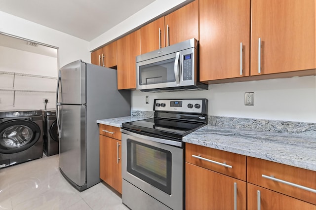 kitchen featuring brown cabinetry, independent washer and dryer, light stone countertops, and stainless steel appliances