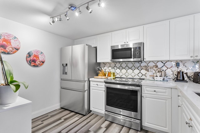 kitchen featuring baseboards, light wood-style flooring, stainless steel appliances, white cabinets, and backsplash