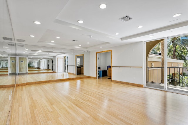 exercise area featuring a raised ceiling, light wood-style floors, and visible vents