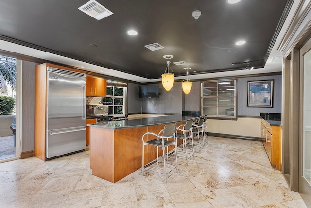 kitchen with a raised ceiling, brown cabinetry, visible vents, and stainless steel built in refrigerator