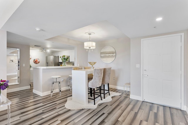 interior space featuring wood finished floors, baseboards, a peninsula, freestanding refrigerator, and a kitchen bar